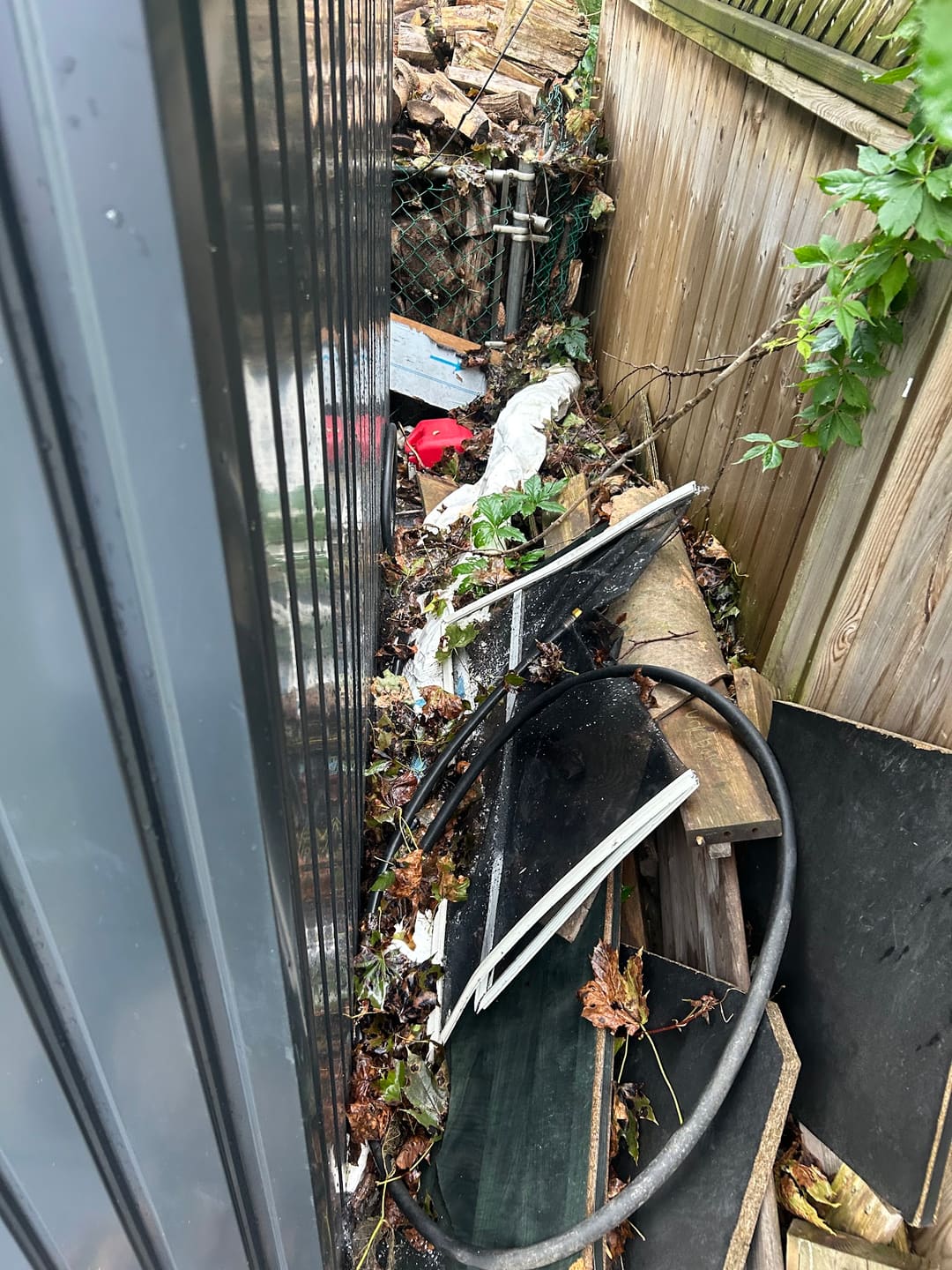 Before: a narrow side yard between a shed and fence, packed with boards, hoses and debris