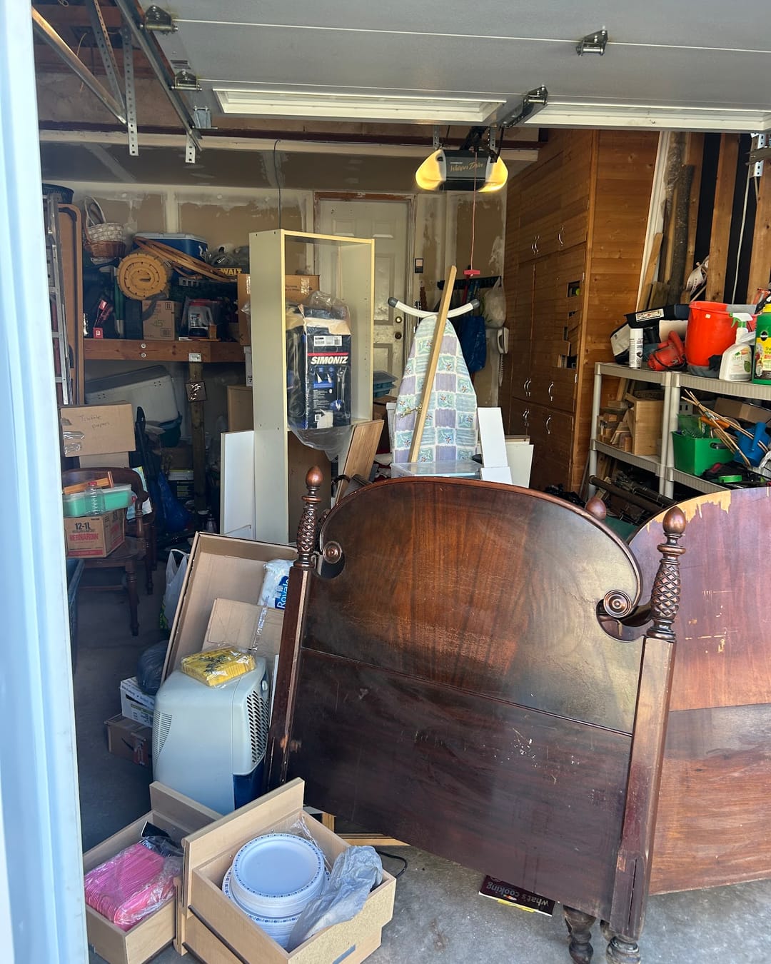 Before: a garage crowded with an old bed frame, boxes and household items